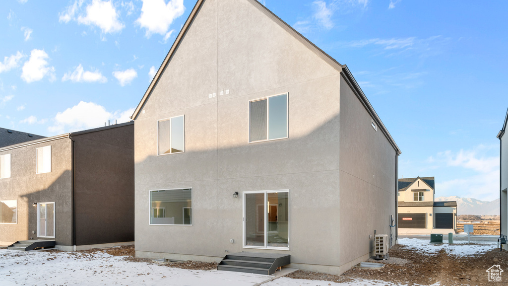 Snow covered rear of property with stucco siding, entry steps, and ac unit