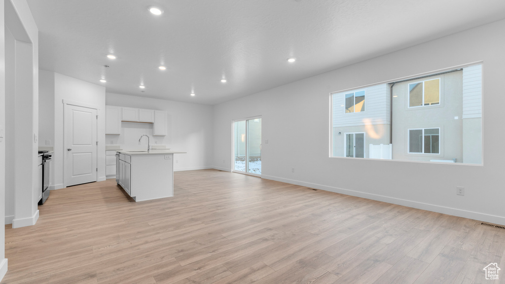 Unfurnished living room featuring a sink, light wood-style floors, recessed lighting, and baseboards