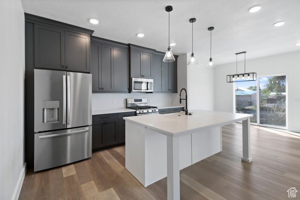 Kitchen featuring appliances with stainless steel finishes, a sink, backsplash, wood finished floors, and light countertops