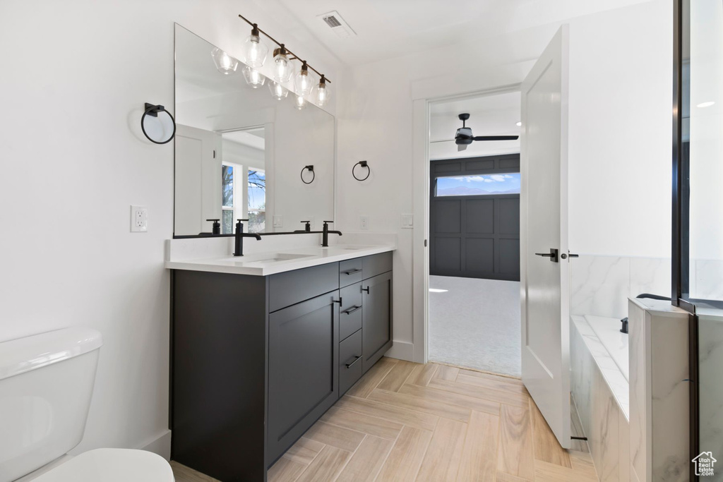 Bathroom featuring toilet, double vanity, ceiling fan, and a bath