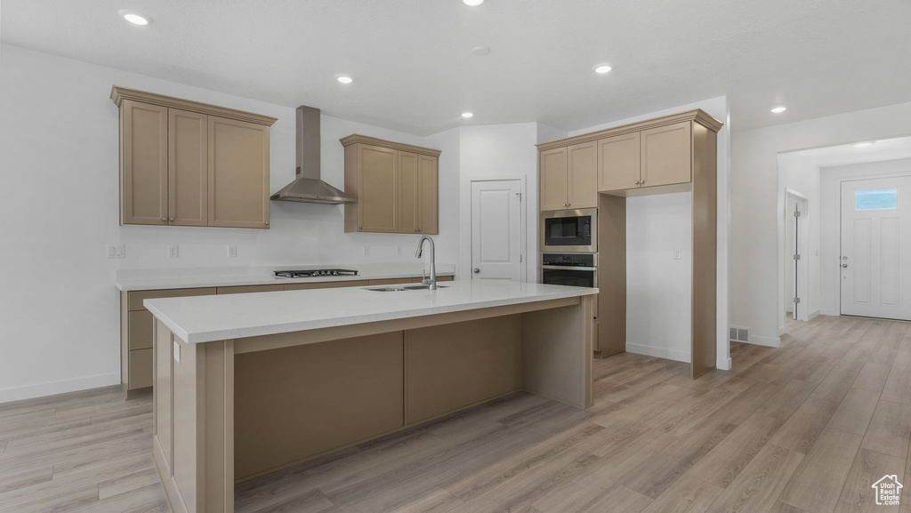 Kitchen with wall chimney range hood, a sink, stainless steel appliances, a kitchen island with sink, and recessed lighting