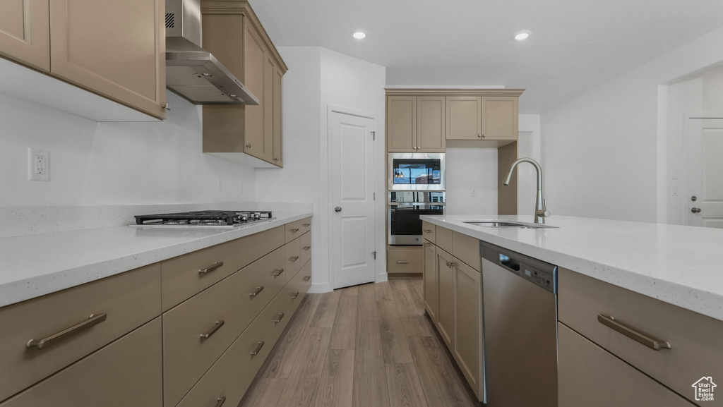 Kitchen with wall chimney range hood, appliances with stainless steel finishes, a sink, light wood-type flooring, and light stone counters