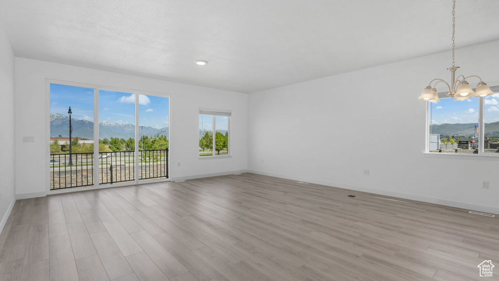 Empty room with a chandelier, light wood-style flooring, a mountain view, and baseboards