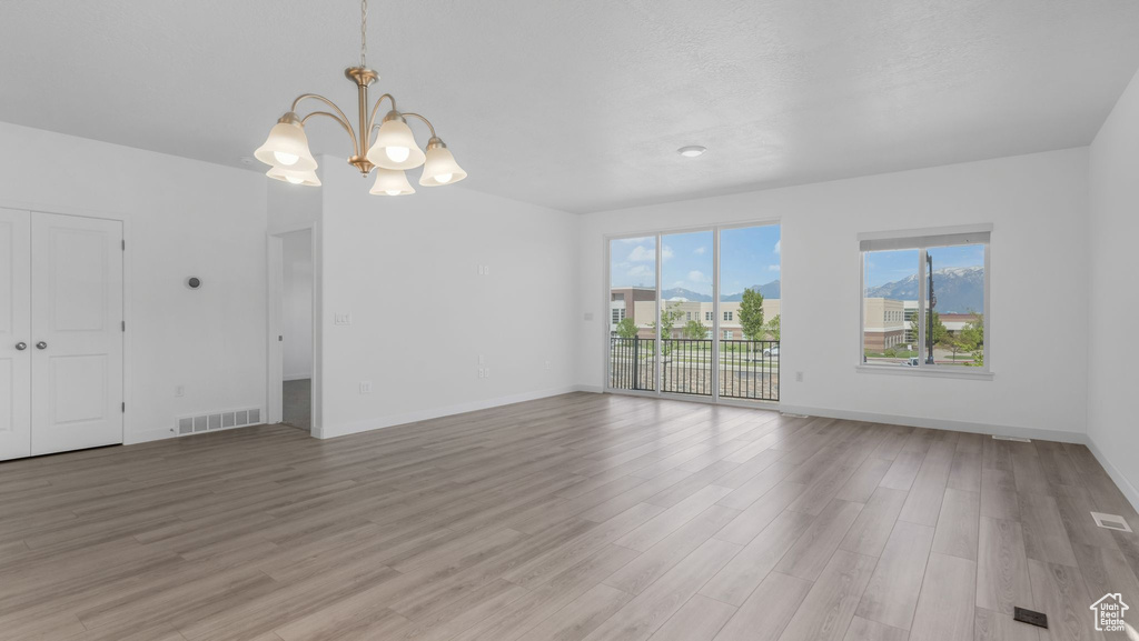 Unfurnished living room featuring a chandelier, light wood-style flooring, and baseboards