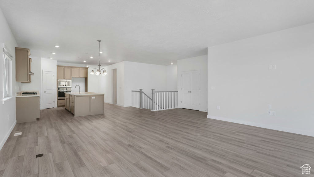 Unfurnished living room featuring a sink, a chandelier, recessed lighting, light wood-style flooring, and baseboards