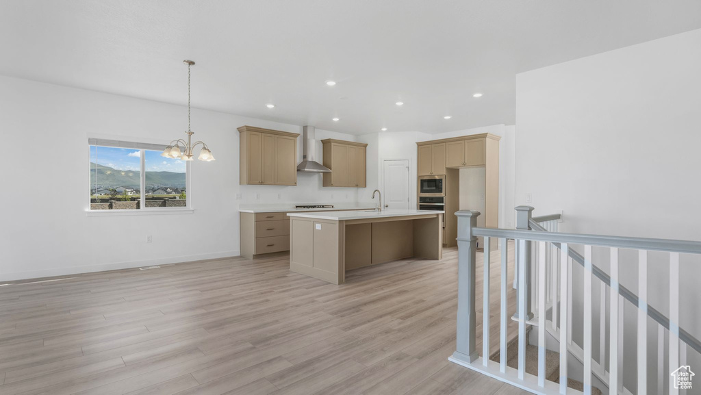 Kitchen featuring stainless steel appliances, a sink, wall chimney range hood, an island with sink, and light countertops
