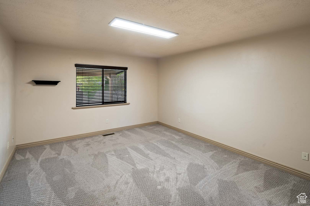 Spare room featuring light colored carpet, baseboards, and a textured ceiling