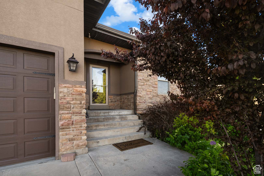 View of exterior entry with stone siding, stucco siding, and a garage