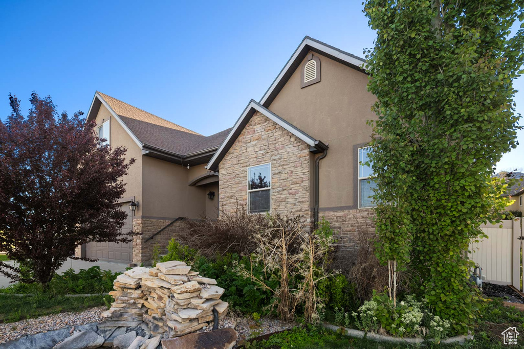 View of property exterior with stone siding, stucco siding, fence, and a garage