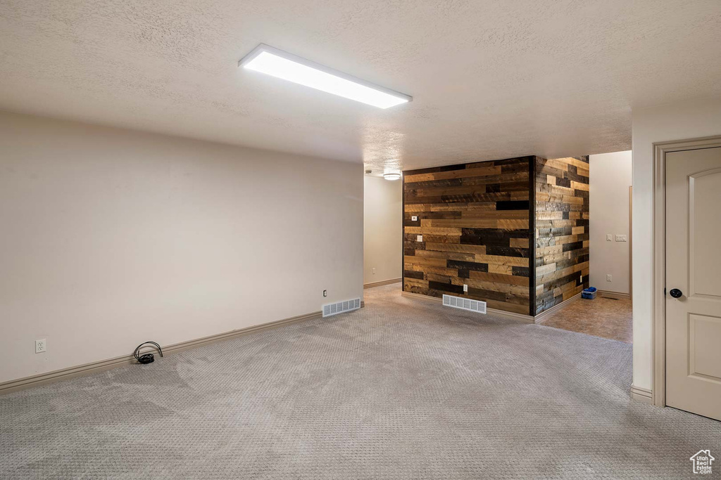 Spare room featuring a textured ceiling, carpet flooring, baseboards, and wooden walls