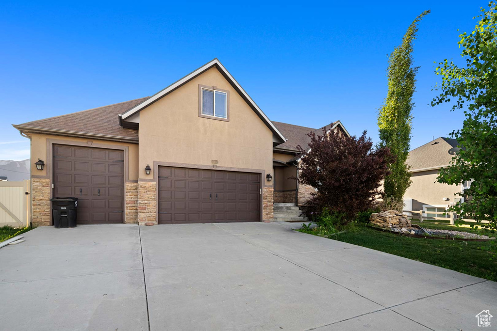 View of front facade with stucco siding, stone siding, driveway, roof with shingles, and a garage