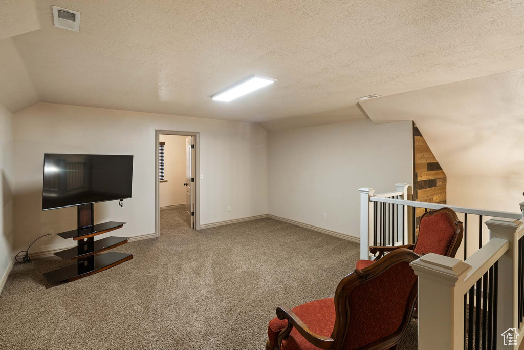 Living area with lofted ceiling, an upstairs landing, carpet, a textured ceiling, and baseboards