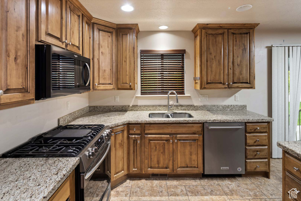 Kitchen with stainless steel appliances, a sink, brown cabinets, light stone counters, and recessed lighting