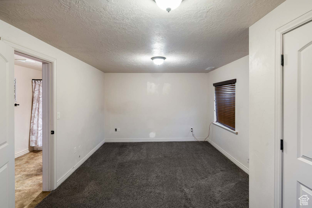 Empty room with a textured ceiling, dark carpet, and baseboards