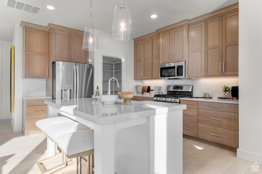 Kitchen featuring appliances with stainless steel finishes, light countertops, recessed lighting, a center island with sink, and decorative light fixtures