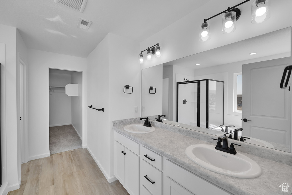 Bathroom with a shower stall, double vanity, wood finished floors, a walk in closet, and baseboards