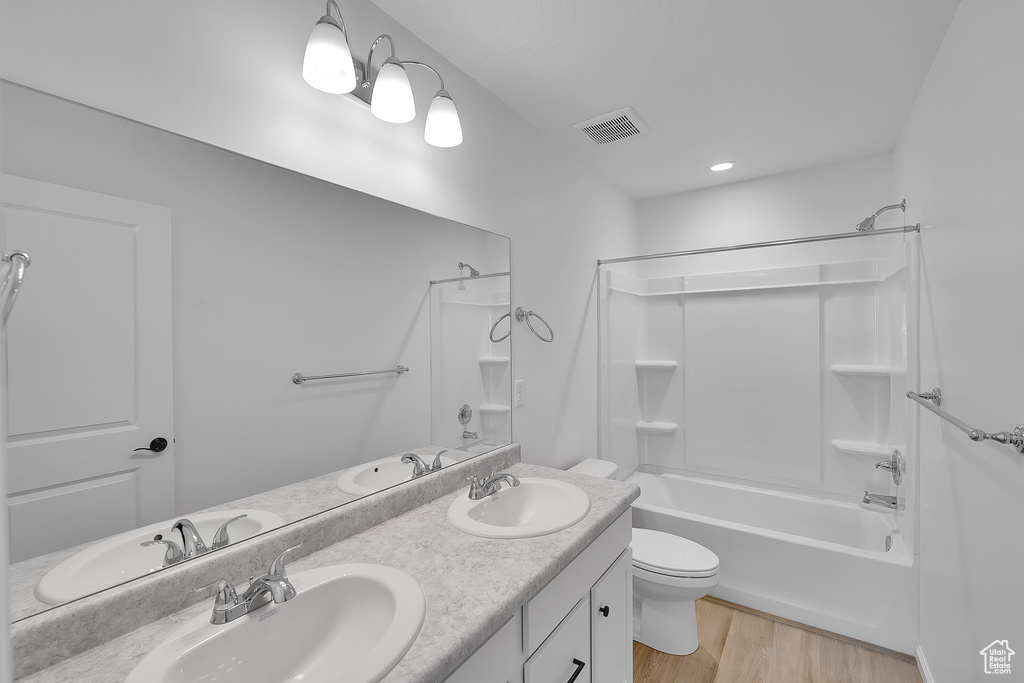 Bathroom with bathtub / shower combination, toilet, wood finished floors, and double vanity