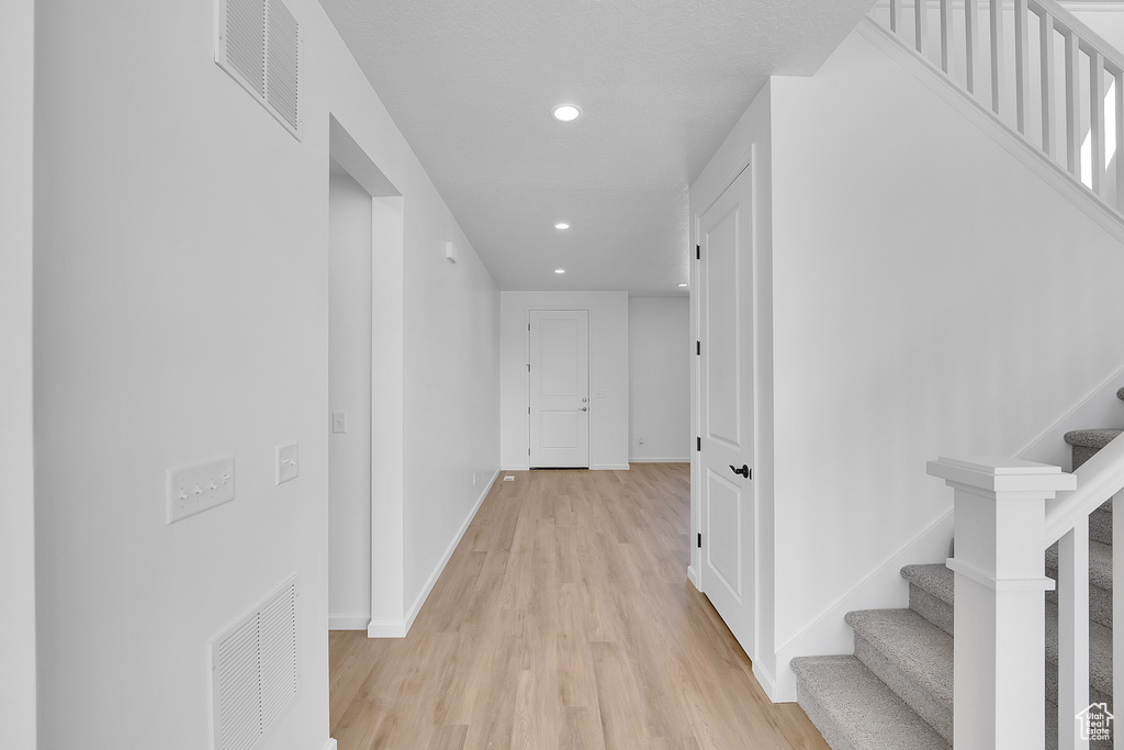 Hallway featuring stairs, light wood-type flooring, recessed lighting, and baseboards