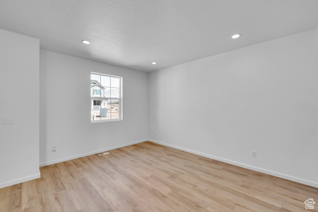Empty room with light wood-style flooring, recessed lighting, baseboards, and a textured ceiling