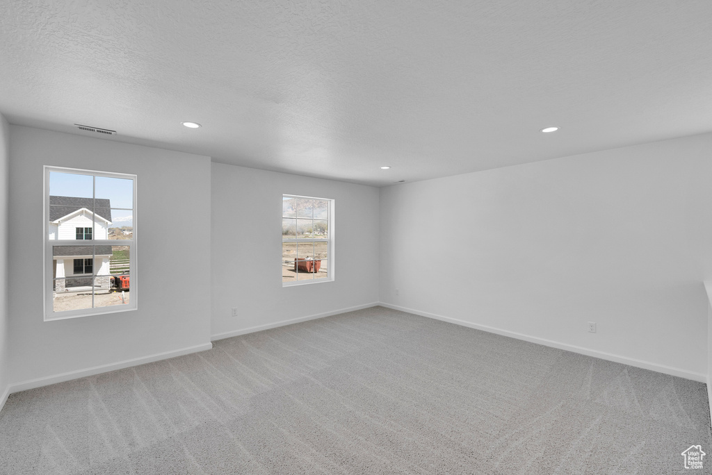 Empty room with light carpet, healthy amount of natural light, recessed lighting, baseboards, and a textured ceiling