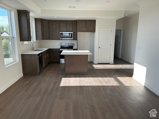 Kitchen with stainless steel appliances, a sink, baseboards, a kitchen island, and dark brown cabinetry