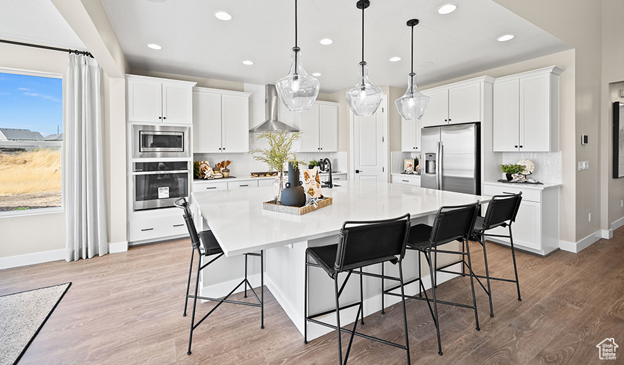 Kitchen featuring stainless steel appliances, wall chimney exhaust hood, recessed lighting, a spacious island, and light wood finished floors