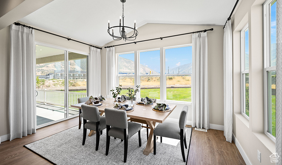 Dining space with vaulted ceiling, healthy amount of natural light, a chandelier, baseboards, and wood finished floors