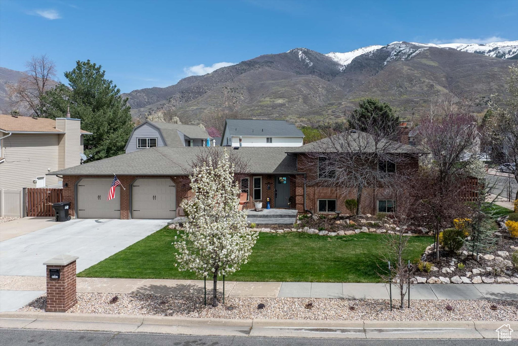 Split level home with a garage, concrete driveway, a mountain view, and brick siding