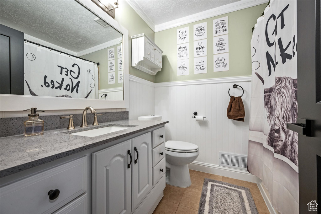 Full bath with a textured ceiling, wainscoting, vanity, ornamental molding, and tile patterned flooring