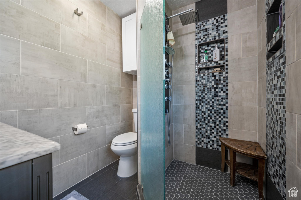 Bathroom featuring tile walls, a stall shower, toilet, vanity, and tile patterned flooring