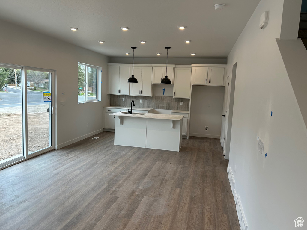Kitchen featuring a sink, baseboards, wood finished floors, backsplash, and a kitchen island with sink