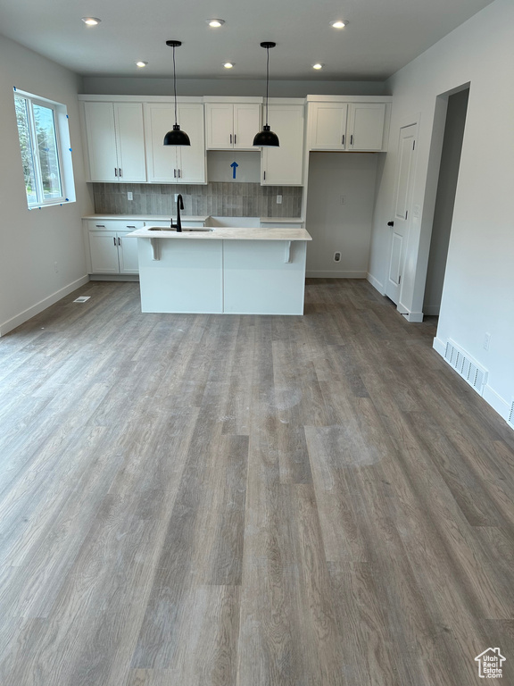 Kitchen with a sink, light countertops, baseboards, wood finished floors, and recessed lighting