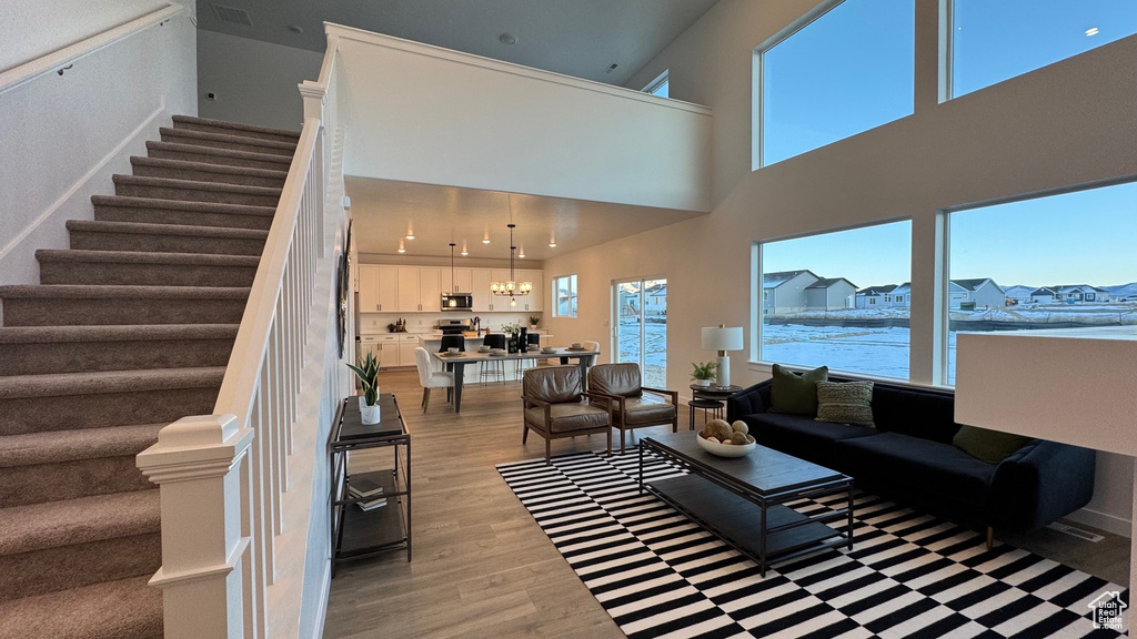Living area with light wood-style flooring, stairway, a towering ceiling, and a chandelier
