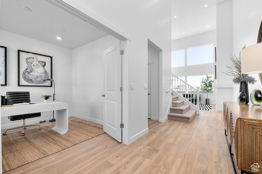 Office space with light wood finished floors, recessed lighting, baseboards, and a towering ceiling