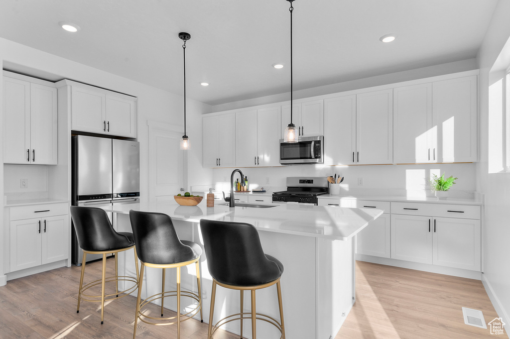 Kitchen with stainless steel appliances, a sink, white cabinets, light countertops, and light wood-style flooring