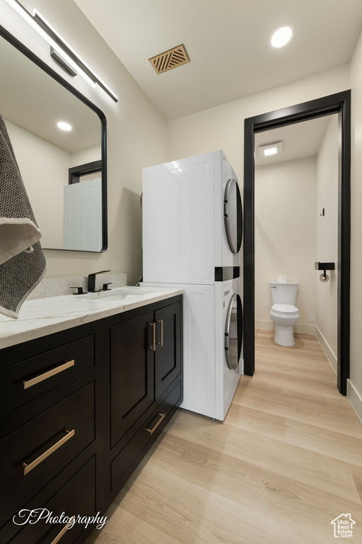 Bathroom featuring estacked washer and dryer, wood finished floors, toilet, baseboards, and vanity