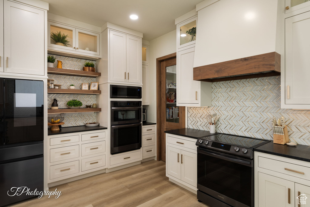 Kitchen with electric stove, custom range hood, built in microwave, tasteful backsplash, and open shelves