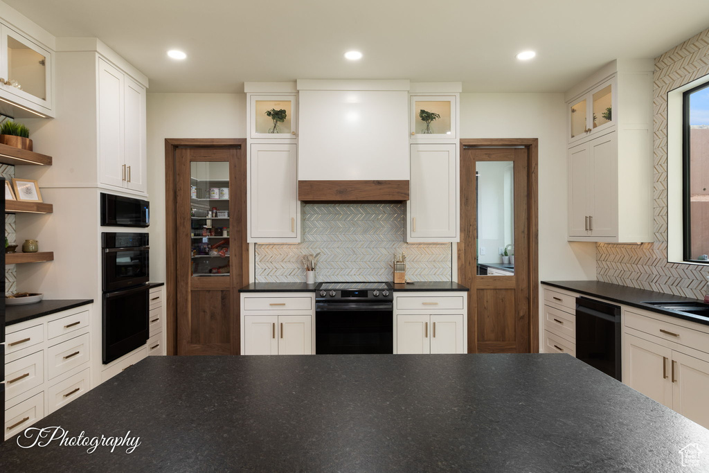 Kitchen with black appliances, dark countertops, tasteful backsplash, custom exhaust hood, and recessed lighting