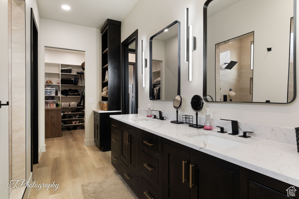 Bathroom featuring wood finished floors, a spacious closet, double vanity, and a shower