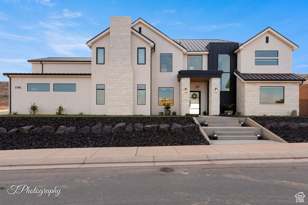 View of front facade featuring a standing seam roof, stucco siding, metal roof, and stone siding