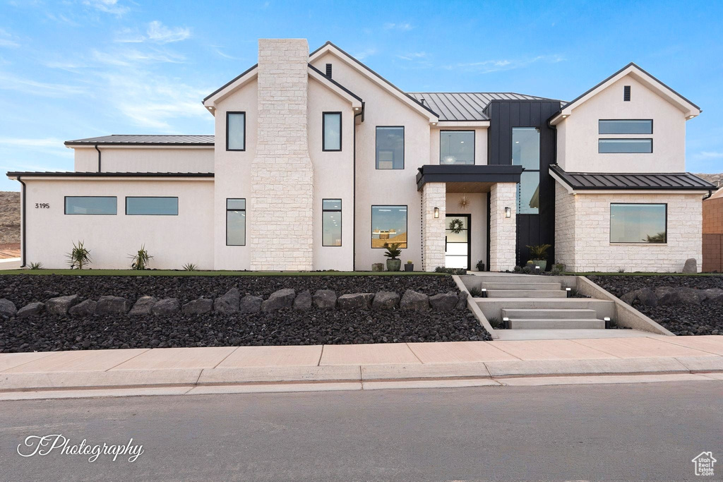View of front of house featuring a standing seam roof, stone siding, a metal roof, and stucco siding