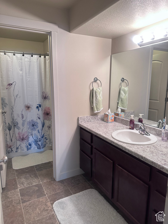 Full bath featuring vanity, a textured ceiling, baseboards, and curtained shower