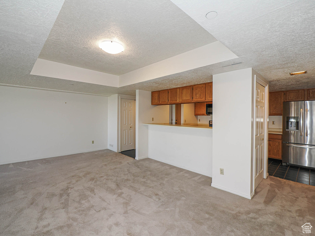 Unfurnished living room with a textured ceiling, carpet flooring, baseboards, and a tray ceiling