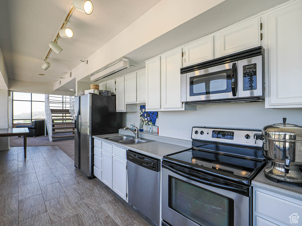 Kitchen with stainless steel appliances, a sink, white cabinets, and track lighting