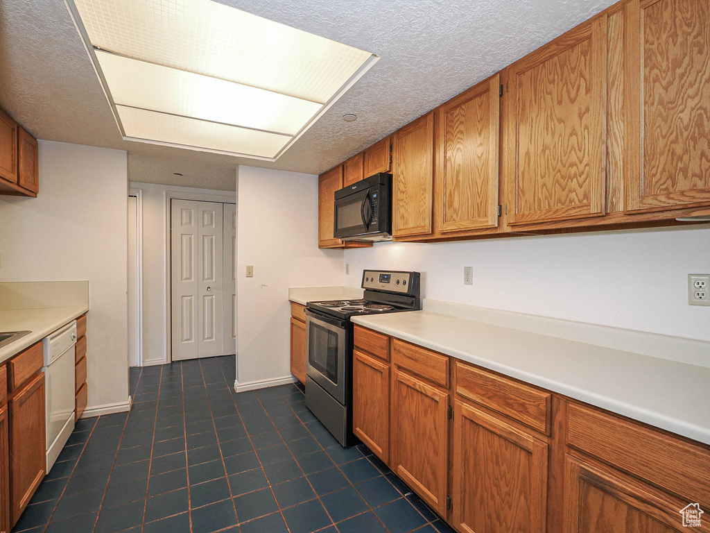 Kitchen with stainless steel electric range oven, black microwave, white dishwasher, brown cabinets, and a textured ceiling