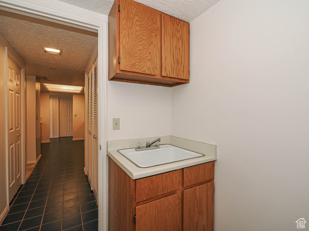 Hall featuring a textured ceiling, a sink, and dark tile patterned flooring