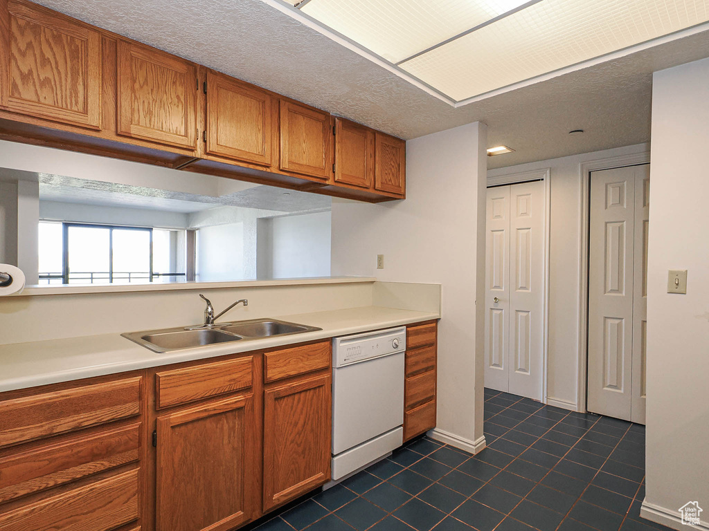 Kitchen with white dishwasher, a sink, dark tile patterned floors, brown cabinetry, and light countertops