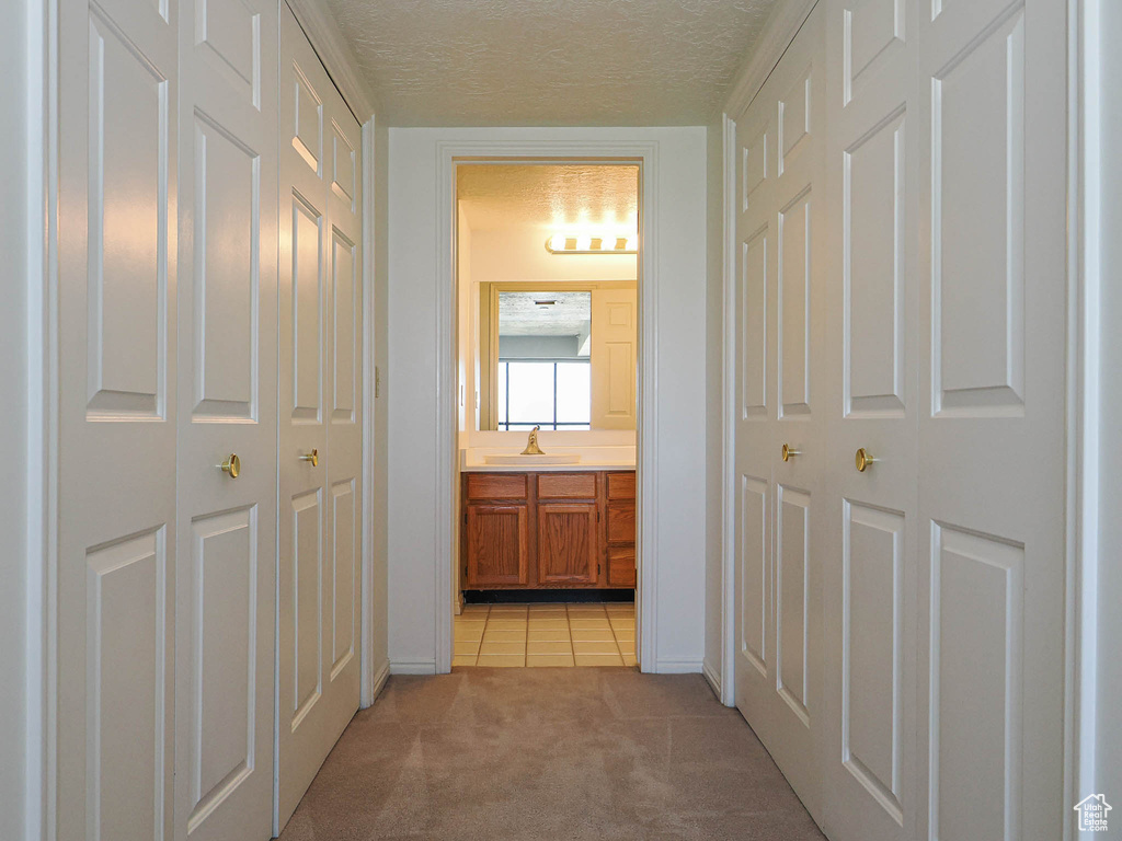 Corridor with light carpet, a textured ceiling, light tile patterned floors, a sink, and baseboards