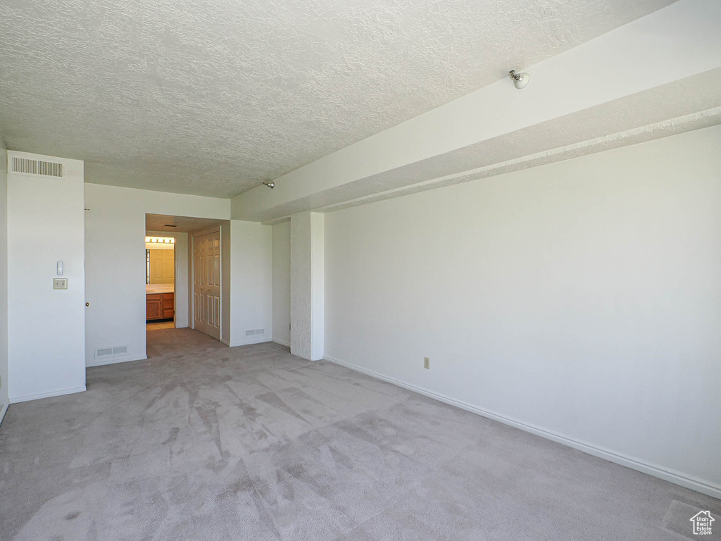 Unfurnished room featuring a textured ceiling, light carpet, and baseboards