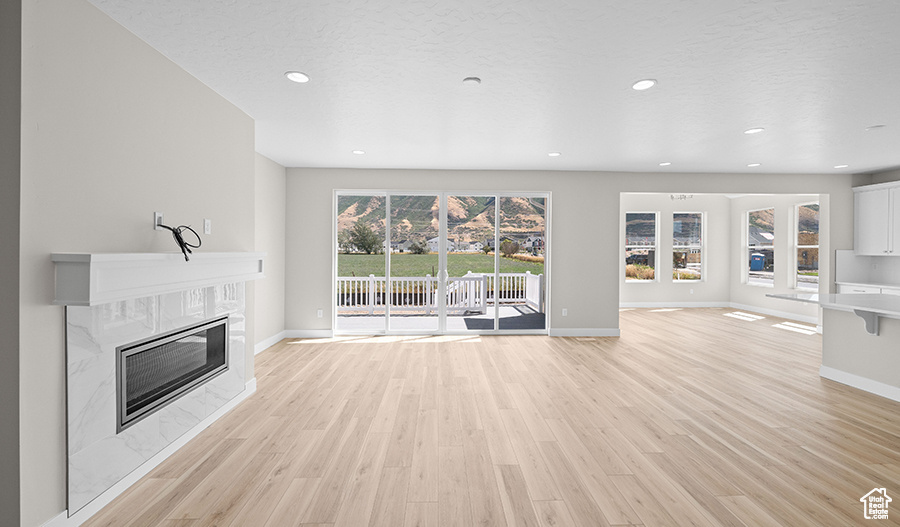 Unfurnished living room featuring light wood-type flooring, a premium fireplace, baseboards, and recessed lighting